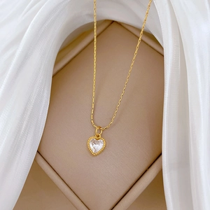 Detail of a golden heart zircon pendant on a necklace, displayed on a beige jewelry box