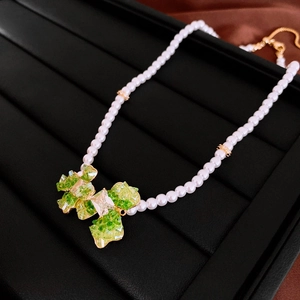 Detail of crystal flower pendant with green stones and pearl necklace on silk background