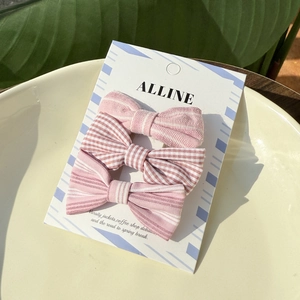 Close-up of three pink striped fabric bow hair clips displayed on a ceramic tray