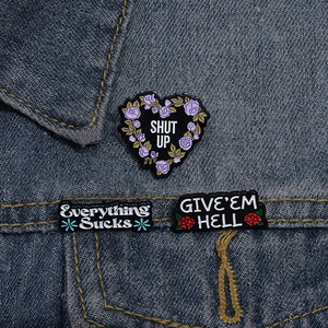 Trois pin's en émail avec citations amusantes fixés sur une poche de veste en jean