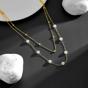 Detail of a double-layered gold stainless steel necklace with elegant white pearls and beads
