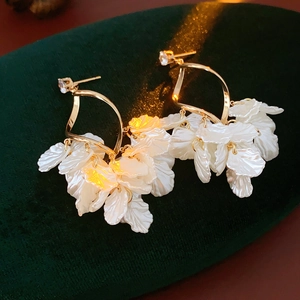 Makro-Detail von eleganten Zirkon-Muschel-Ohrringen mit weißen Blütenblättern auf Samt