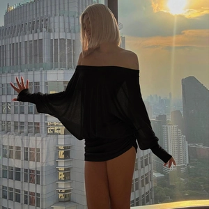 Silhouette d'une robe courte noire à épaules dénudées devant la ville au coucher du soleil