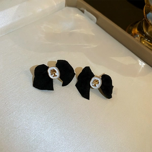 Macro detail of black velvet bow earrings with gold-rimmed white cameo portrait charms