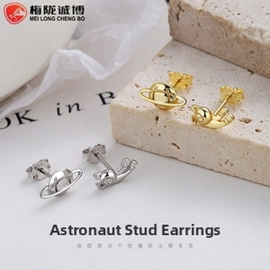 Macro detail of asymmetric astronaut and planet stud earrings in silver and gold