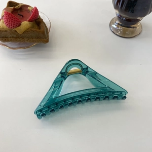 Detail showing transparent green large triangle hair claw clip with golden spring on a desk