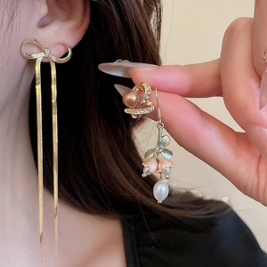 Detailed close-up of asymmetrical flower and pearl drop earrings with elegant gold tassels