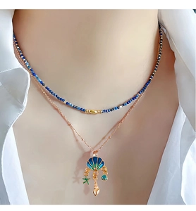 Detail of layered gold necklace featuring a blue shell pendant and marine charms