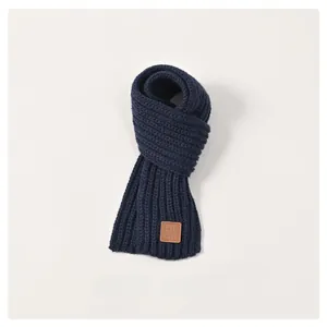 Detail of dark blue knit scarf for children with a vintage brown leather logo patch