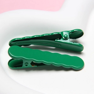 Detail view of two dark green wave-shaped metal hairpins on a heart-shaped tray
