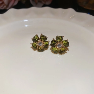 Close-up of green flower stud earrings with center diamond on a decorative ceramic dish
