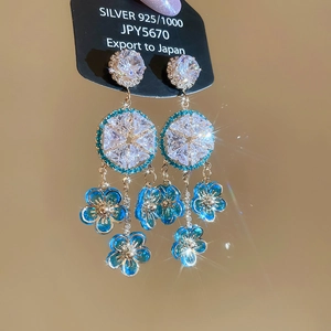 Detail view of silver fringe earrings with blue flowers and sparkling crystals