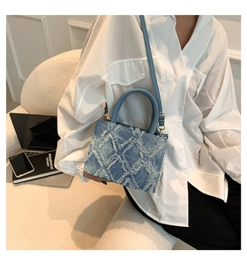 Close-up of blue denim tote bag with quilted fringe texture and leather strap in office setting