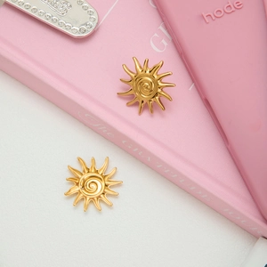 Gros plan de boucles d'oreilles soleil dorées 18 carats avec centre en spirale sur carnet