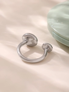 Détail d'une bague ouverte argentée avec deux plaques rondes sur un fond beige doux