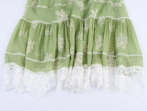 Detail of green fabric dress with white embroidery and wide lace hemline