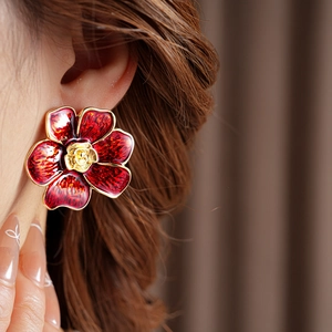 Primer plano de pendientes vintage de flores rojas con bordes dorados en modelo