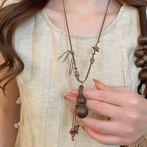 Detail shot of vintage wooden gourd pendant necklace on linen clothing for women