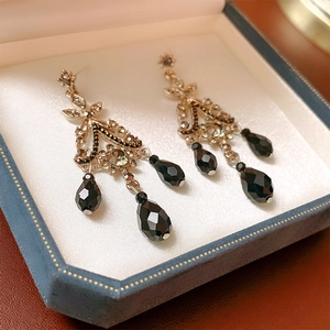 Detailed close-up of vintage gold earrings with crystal inlay and black teardrop charms