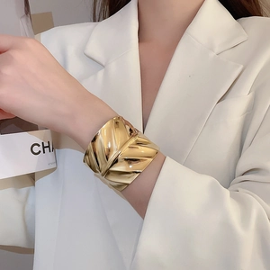 Gros plan du bracelet manchette doré à texture ondulée porté par un mannequin chic