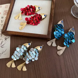 Three pairs of elegant fish-shaped hair clips with shell scale texture on dark wood background