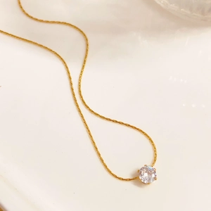 Macro detail of gold six-prong necklace with a brilliant round-cut sparkling zircon stone