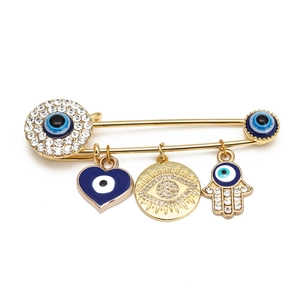 Detail of gold safety pin brooch with Hamsa Hand and Evil Eye crystal charms