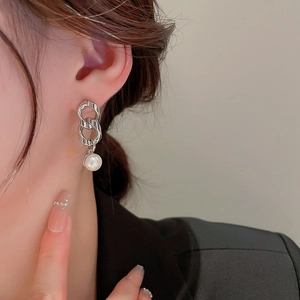 Close-up of silver chain earring with white pearl drop on model's ear in minimalist style