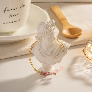 Artistic display of gold beaded bracelet with colorful stones on a white bust statue