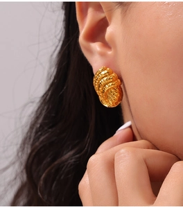 Vue macro de boucles d'oreilles dorées texturées avec design ondulé sur un mannequin