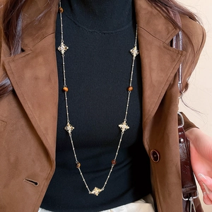 Detail of vintage tiger eye cross necklace styled on a brown suede coat and black top