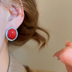 Detail of red oval stud earring with silver frame worn on ear for a luxury look