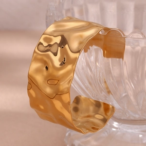 Macro detail of 18K gold plated hammered texture cuff bracelet on a glass display