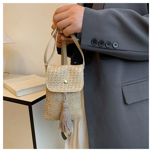 Close-up of beige woven straw crossbody bag with fringe tassel and metallic snap