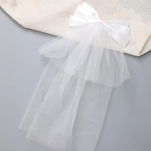 Detail of white satin bow hair clip with a long tulle veil on beige knit fabric background