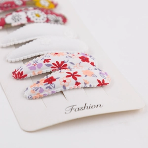 Detail of floral embroidery on soft fabric hair clips set against white background