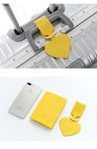 Macro view of heart-shaped yellow leather luggage tag on a silver suitcase handle