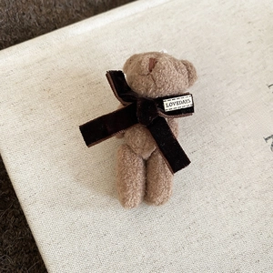 Close-up of a flocking teddy bear brooch with velvet bow and LOVEDAYS woven label detail