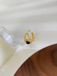 Detailed shot of 18K gold ring with black natural stone and textured band on wooden plate