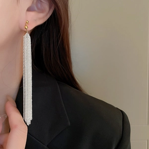 Detailed view of long metallic chain fringe earrings worn by a model in a black suit