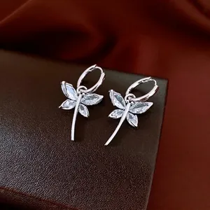 Elegant silver dragonfly earrings with marquise-cut zircon wings on premium leather surface