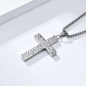 Gros plan du pendentif croix argenté à texture martelée avec chaîne à mailles