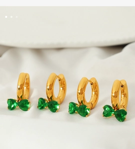 Close-up of gold hoop earrings with green zircon bow charms on white fabric