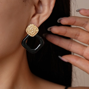 Macro detail of geometric earrings featuring hammered gold metal and black resin link