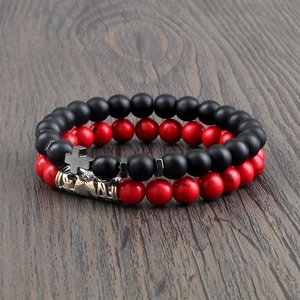 Detail view of beaded bracelet set with matte black beads, metal cross, and red marble beads