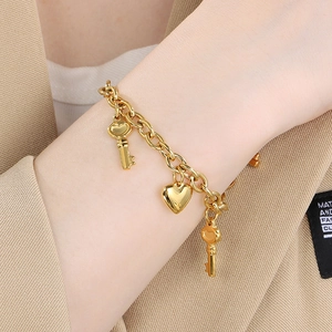 Golden heart and key pendant chain bracelet shown on wrist with khaki suit background