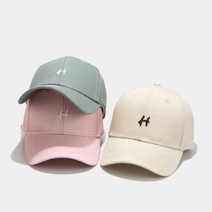 Tre berretti da baseball ricamati con lettera H in verde, rosa e beige su sfondo bianco