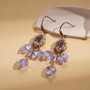 Vintage bohemian drop earrings with purple beads and tassel detail on textured background