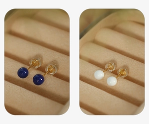Close-up of small round stud earrings in deep blue and white with gold finish