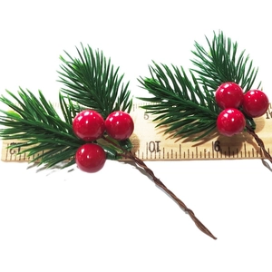Top view of two artificial Christmas pine branches with red berries measured on a wooden ruler